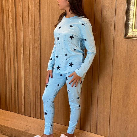 Woman wearing a light blue pyjama set with black star patterns against a wooden wall