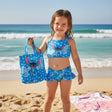Girl wearing a blue Stitch print swimsuit set holding a matching tote bag on the beach