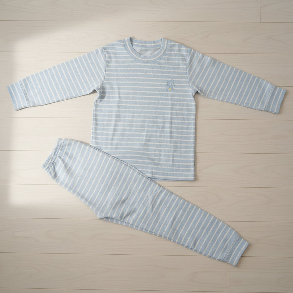 Light blue and white stripe kids pyjama set laid flat on a wood floor, crew neck top with joggers