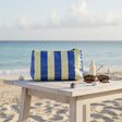 Blue and white striped beach bag on a wooden table with sunglasses and a bottle of sunscreen, set against a beach backdrop.