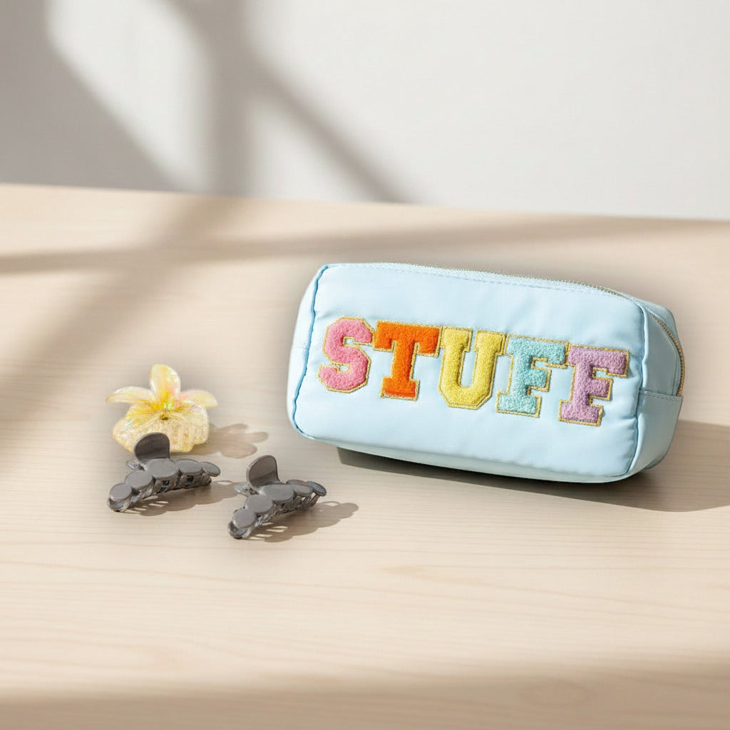 Blue pouch with colorful 'STUFF' text on a beige surface with flowers and hair clips
