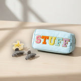 Blue pouch with colorful 'STUFF' text on a beige surface with flowers and hair clips