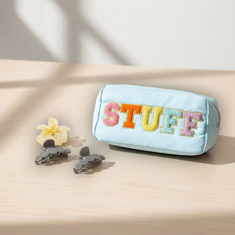 Blue pouch with colorful 'STUFF' text on a beige surface with flowers and hair clips
