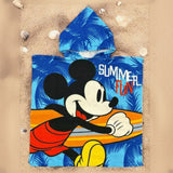 Blue Mickey Mouse poncho towel with palm leaves and a surfboard print flat lay on sand