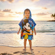 Boy on the beach in a blue Mickey Mouse poncho towel with a surfing print