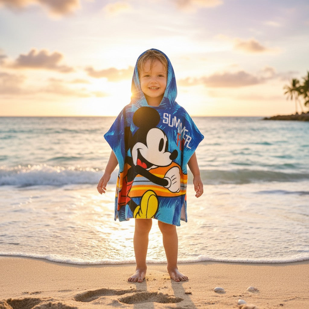 Boy on the beach in a blue Mickey Mouse poncho towel with a surfing print