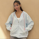 Baby blue hoodie zipped to the chin against a warm tan backdrop