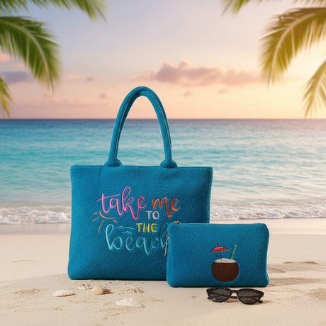 Blue tote bag with 'take me to the beach' text and matching pouch on a beach with sunset.