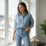 Woman wearing a light blue denim outfit standing in a bright room with large windows