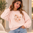 Woman in a blush pink crew neck sweatshirt with an orange hand drawn tulip print and light wash jeans