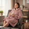 Woman relaxing in an armchair wearing a blush pink hooded blanket with teddy bear embroidery