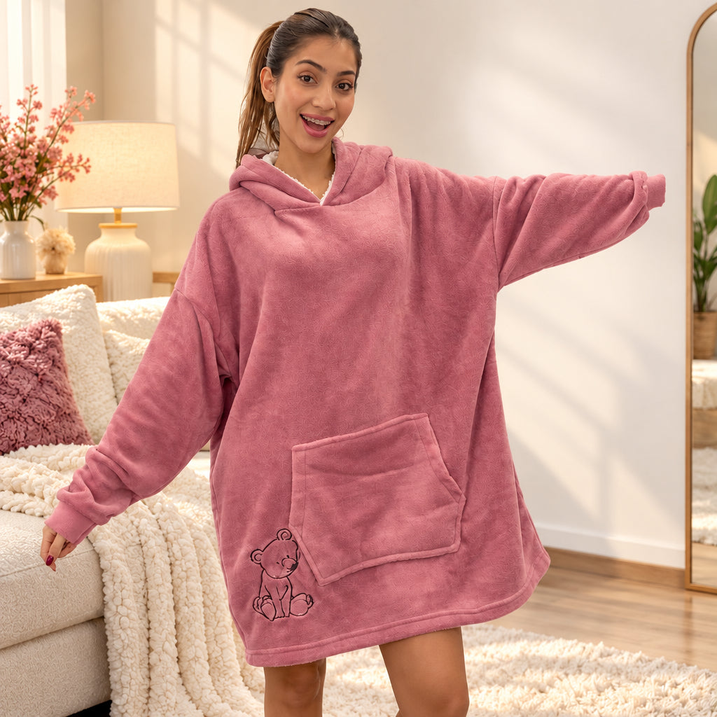 Woman in a mauve blush fleece hooded blanket with a bear outline, arm stretched out in a bright living room