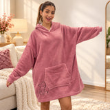 Woman in a mauve blush fleece hooded blanket with a bear outline, arm stretched out in a bright living room
