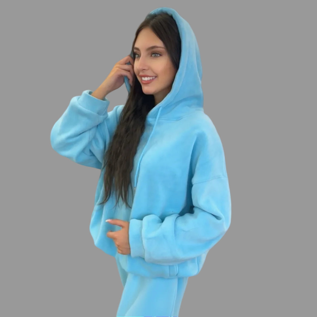 Woman wearing a blue hoodie and sweatpants against a gray background