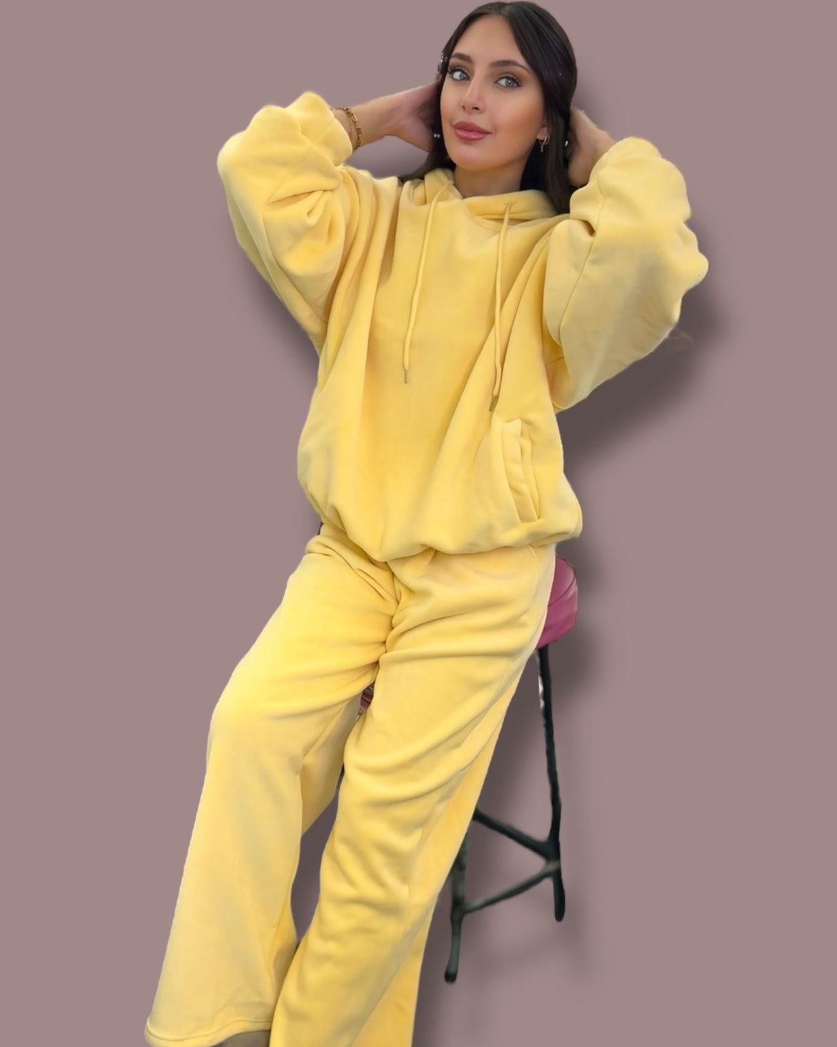 Person wearing a yellow jogging set sitting on a stool against a plain background