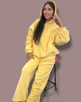 Woman wearing a yellow jogging set sitting on a chair against a plain background