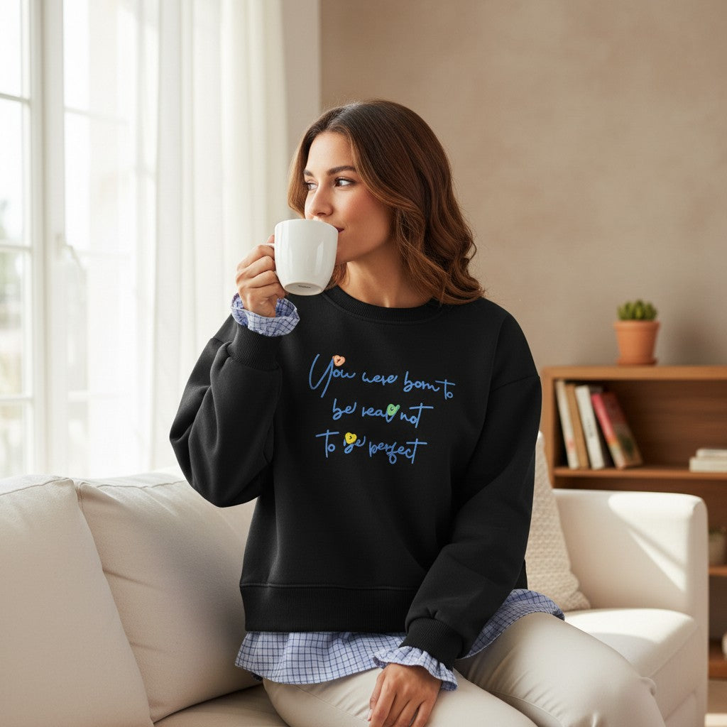 Woman drinking from a white mug on a sofa in a black sweatshirt with gingham trim