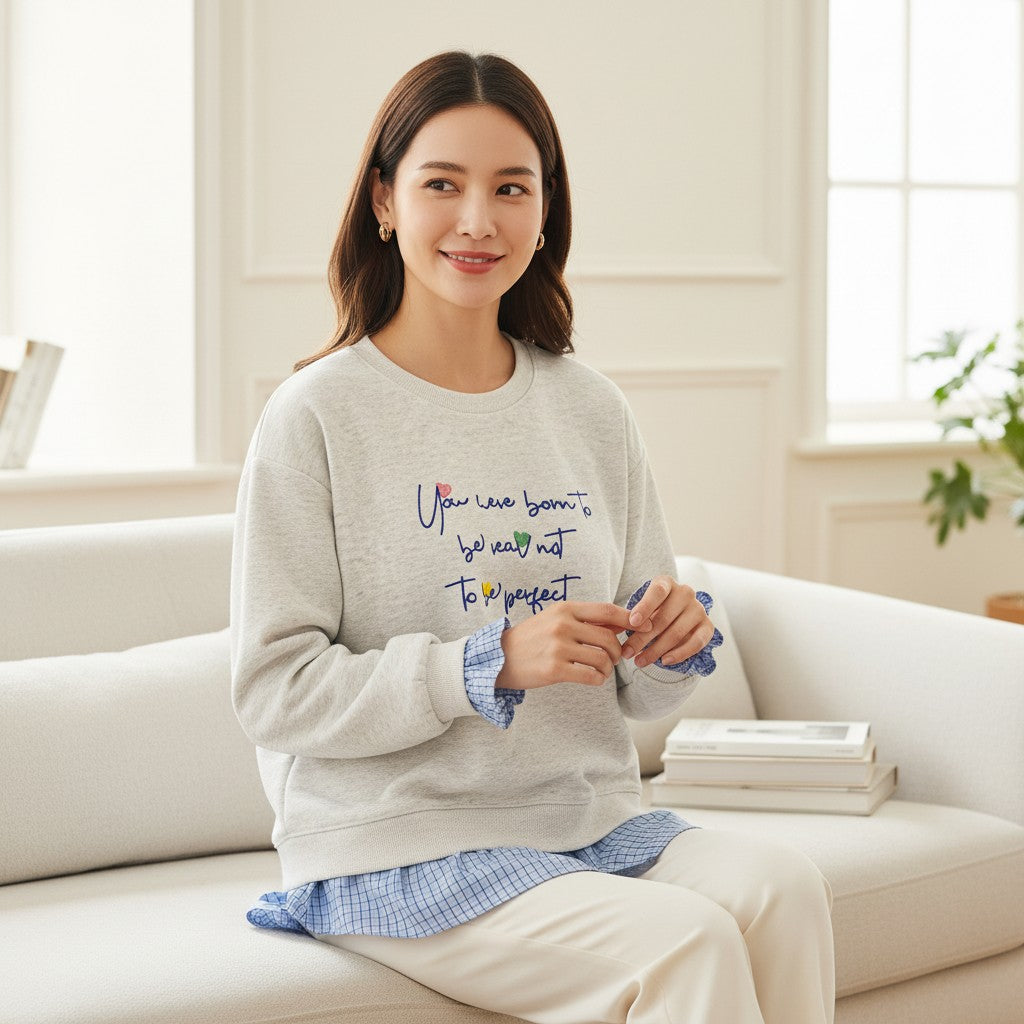 Smiling woman on a cream sofa in a heather grey sweatshirt over gingham layers