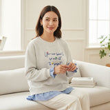 Smiling woman on a cream sofa in a heather grey sweatshirt over gingham layers