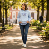 Walking a leafy avenue in a light blue embroidered sweatshirt and dark jeans