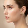 Close-up of a woman wearing a gold bow-shaped earring against a beige background