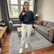 Woman wearing a black sweater with bow details and grey sweatpants in a living room