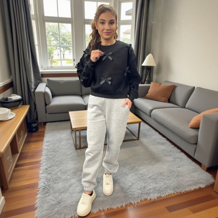 Woman wearing a black sweater with bow details and grey sweatpants in a living room