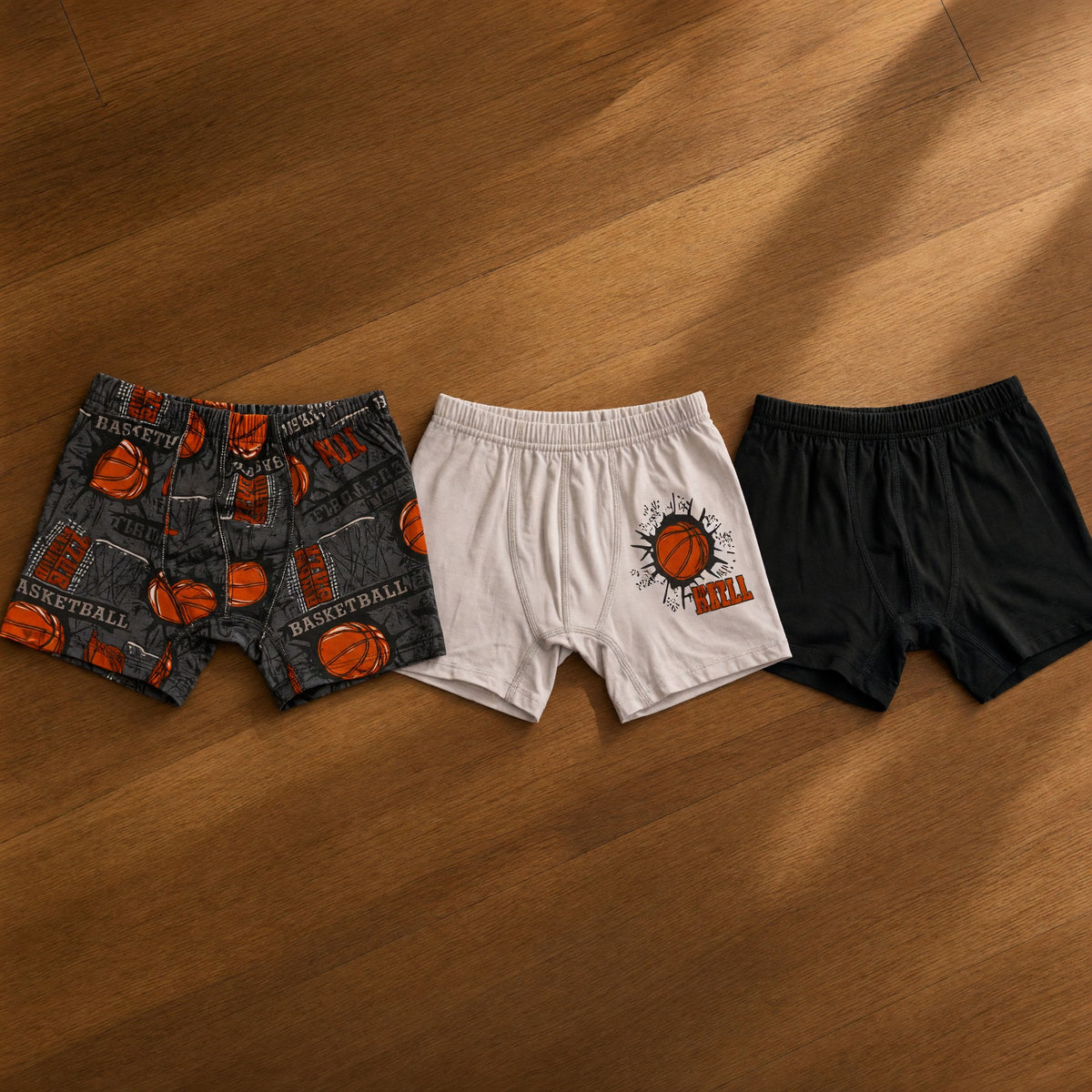 Three boys boxers in a charcoal basketball print, light grey with an orange ball graphic and plain black