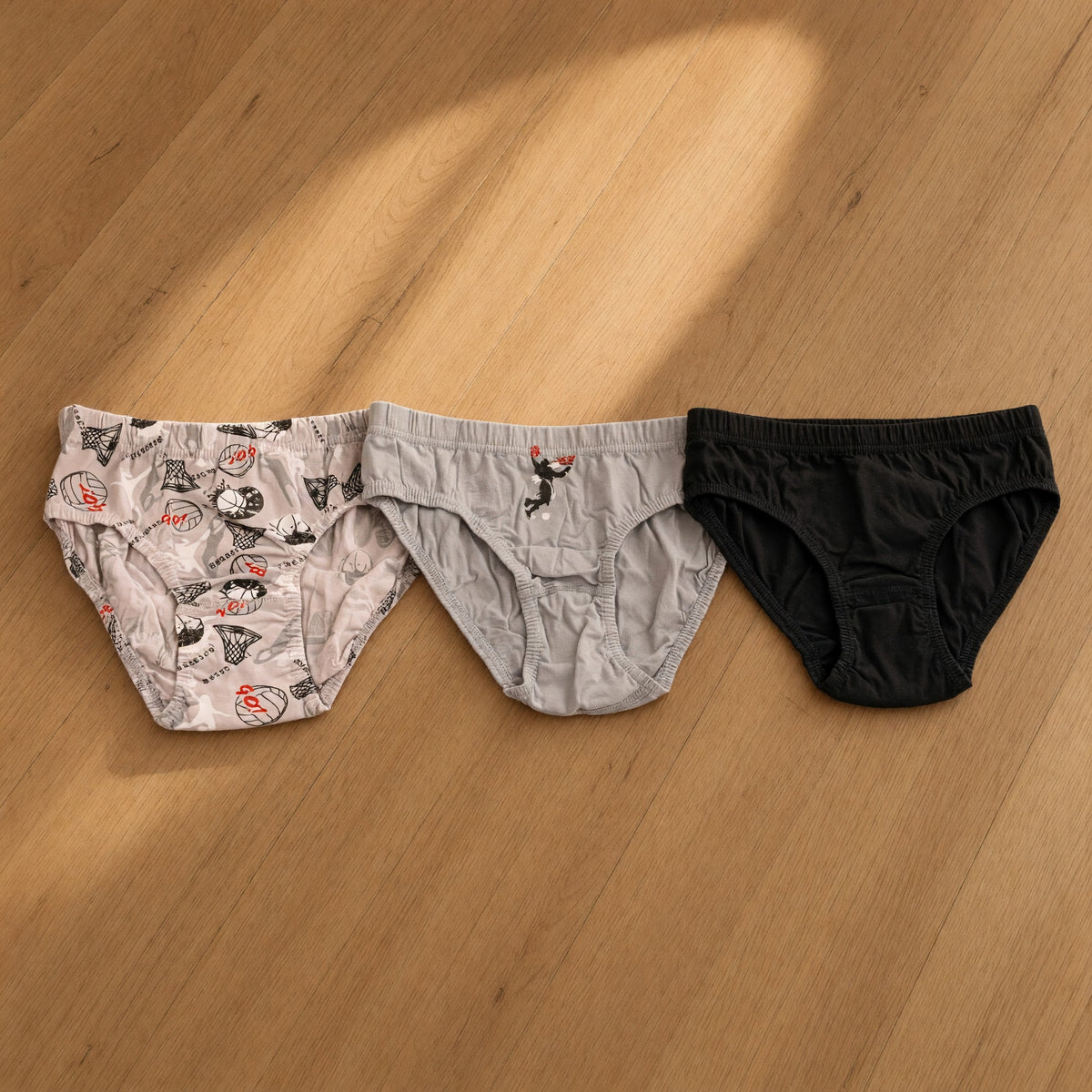 Three boys briefs in a grey basketball print, plain grey with a player graphic and plain black