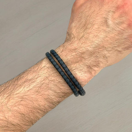 Black and blue braided leather bracelet on a wrist against a grey background
