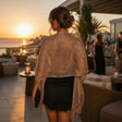 A woman stands on a rooftop terrace wearing a shimmering bronze classy scarf over a black ruffled mini dress