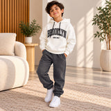 Boy in a white Brooklyn varsity hoodie and dark grey joggers in a living room