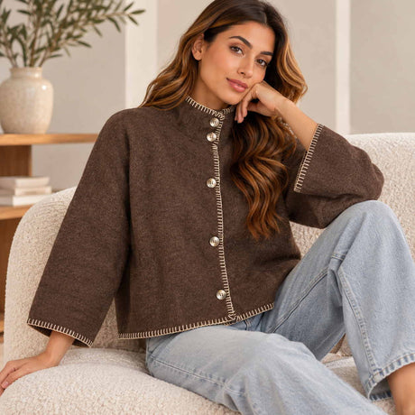 Brown cropped wool cardigan with cream blanket stitch trim and a stand collar, worn on a boucle chair