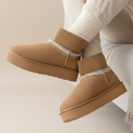 Brown winter boots with patterned trim worn by a person sitting on a couch