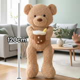 Full height view of the tan curly teddy against a 120cm scale, its pearl dotted drink plush in one arm
