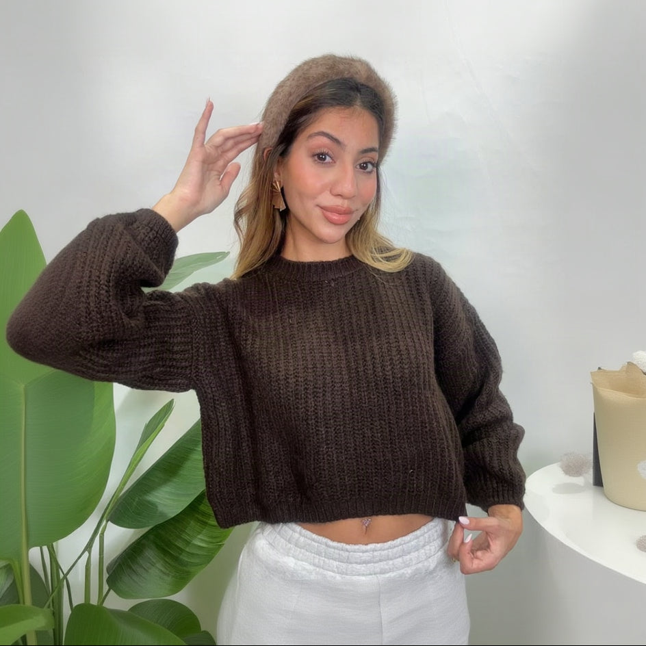 Woman in a chocolate brown chunky ribbed knit cropped sweater with balloon sleeves and a furry headband