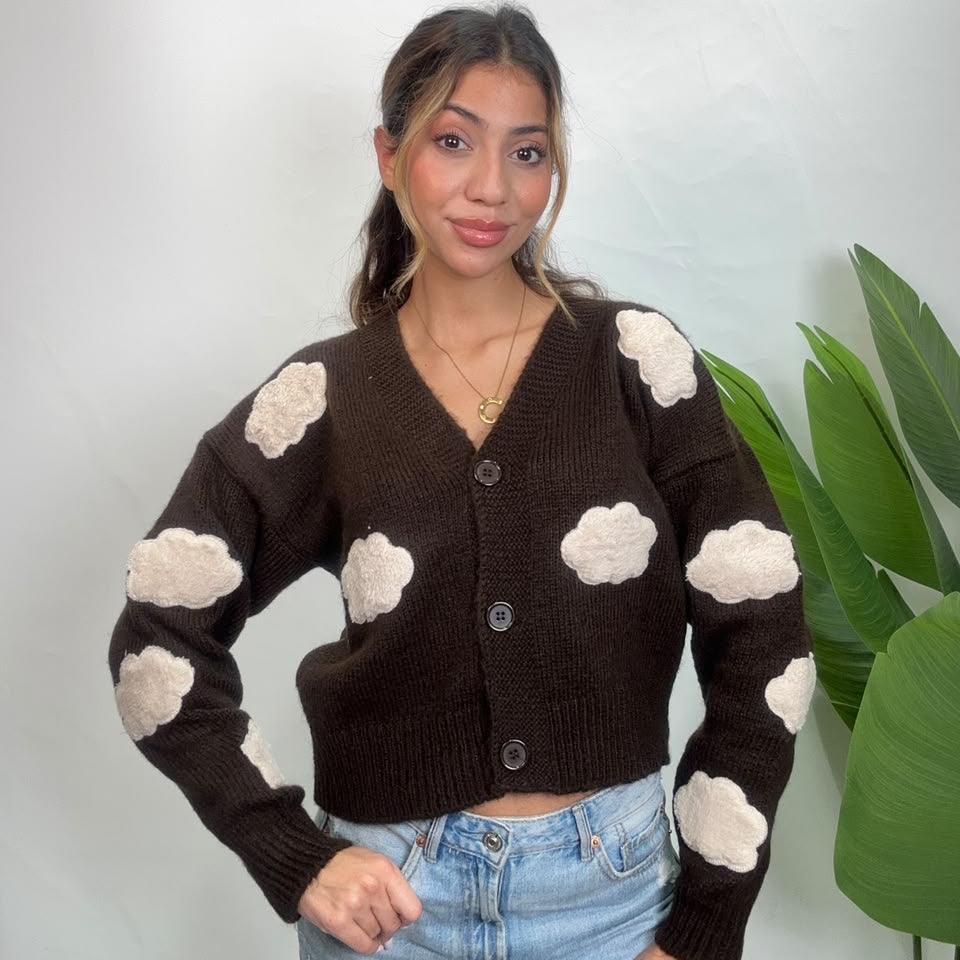 Woman in a dark brown V neck cardigan with cream cloud patches and buttons, worn with jeans