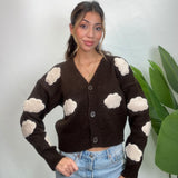 Woman in a dark brown V neck cardigan with cream cloud patches and buttons, worn with jeans