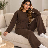 Brown knit jumper and wide leg pants set, worn sitting on a cream boucle sofa with white socks