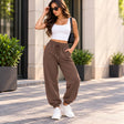 Woman in chocolate brown cuffed joggers with a drawstring waist, a white tank crop top and white sneakers