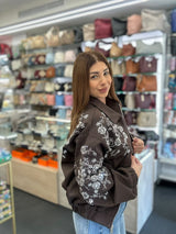 Brown beaded floral bomber jacket worn in a shop in front of shelves of handbags