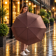 Woman on a rainy pavement holding a brown herringbone folding umbrella open