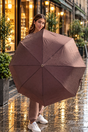Woman on a rainy pavement holding a brown herringbone folding umbrella open