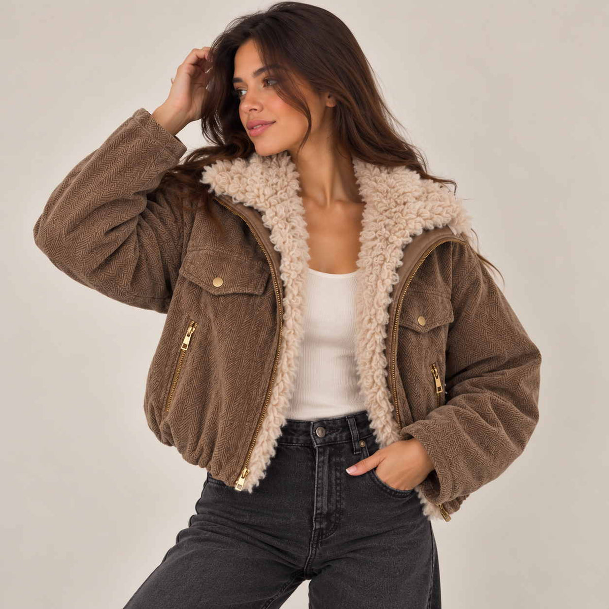 Woman in a brown sherpa collar jacket with gold zip pockets, hand in her jeans pocket