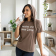Woman wearing a brown hydration tshirt and holding a water bottle with text in a bright room