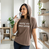 Woman wearing a brown hydration tshirt and holding a water bottle with text in a bright room