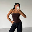 Person wearing a brown top and dark jeans taking a mirror selfie against a plain white wall