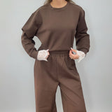 Brown sweatshirt and joggers with hands in the pockets, lace peeking at the cuffs