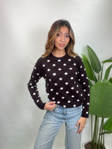 Woman in a dark brown knit sweater with white polka dots and light blue jeans, hand on her hip