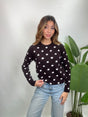 Woman in a dark brown knit sweater with white polka dots and light blue jeans, hand on her hip